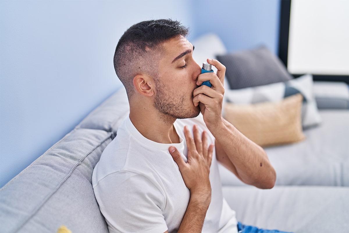 young hispanic man using inhaler sitting sofa home min